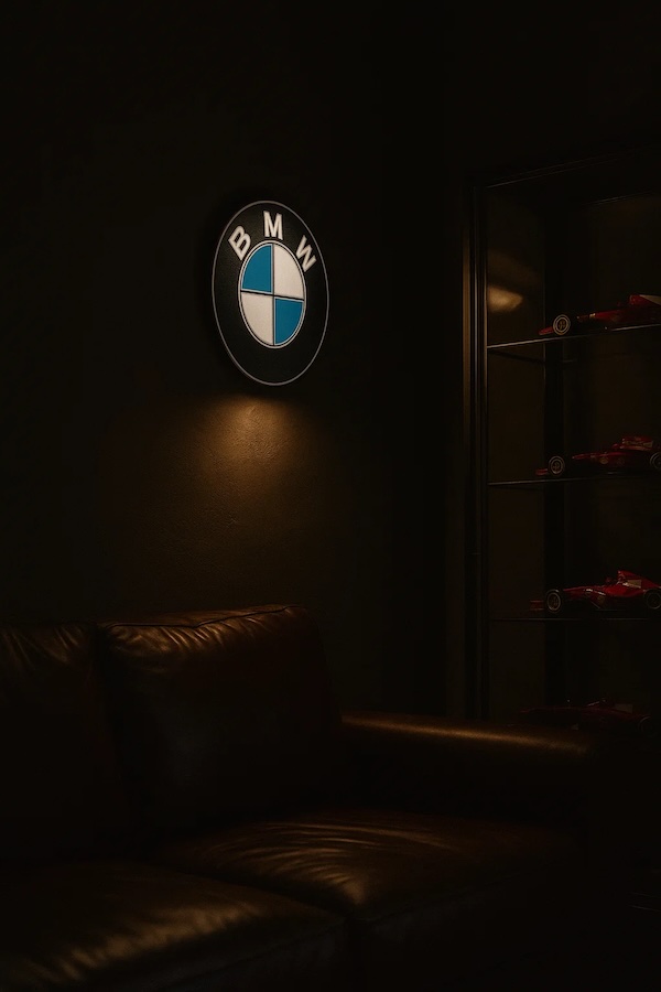 Runde BMW-Logo LED-Lampe in schwarz weiss blau in einem dunklen Zimmer รผber einer Ledercouch neben einer Vitrine